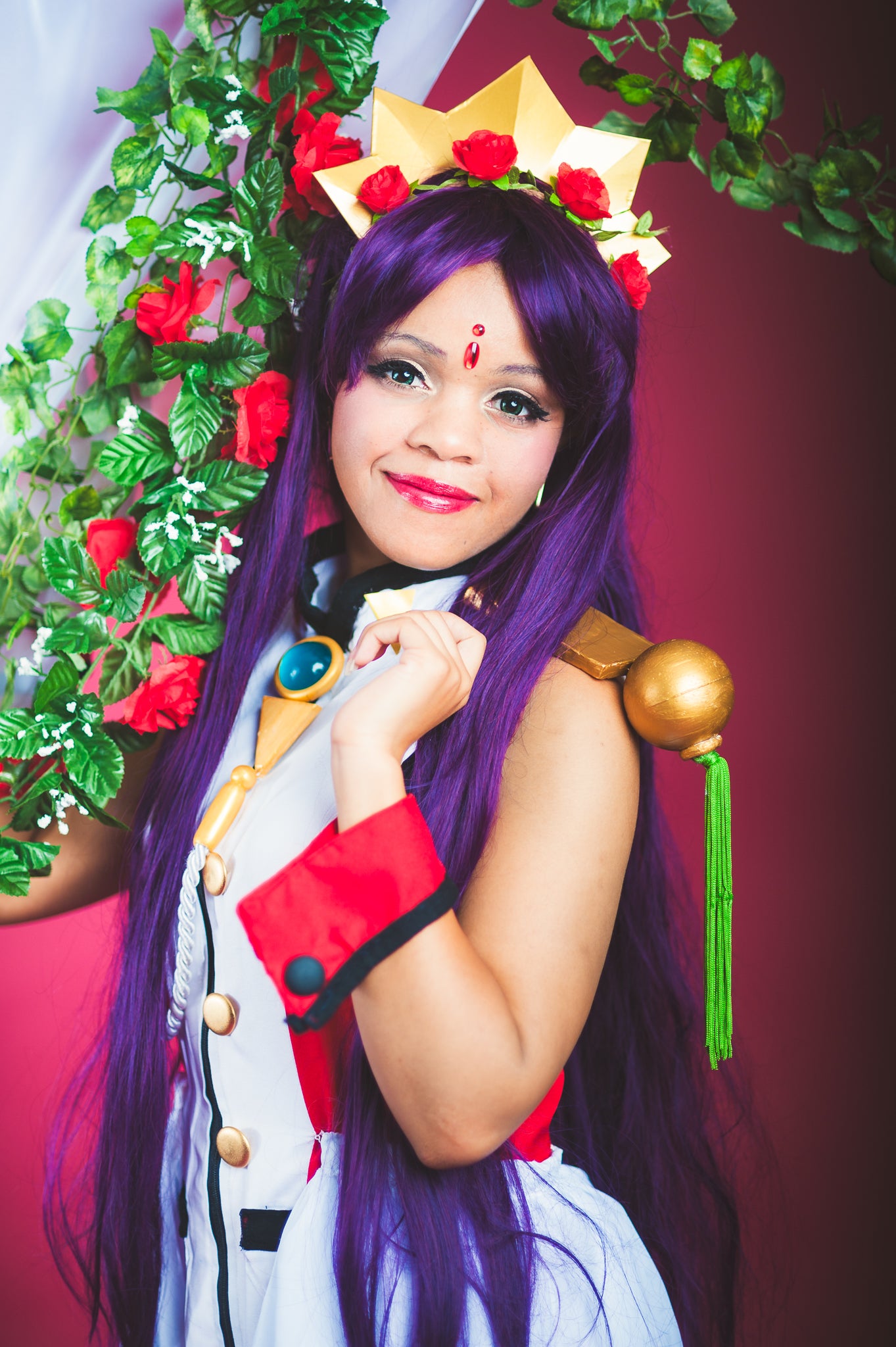 Person with purple hair and costume posing in front of a floral arch