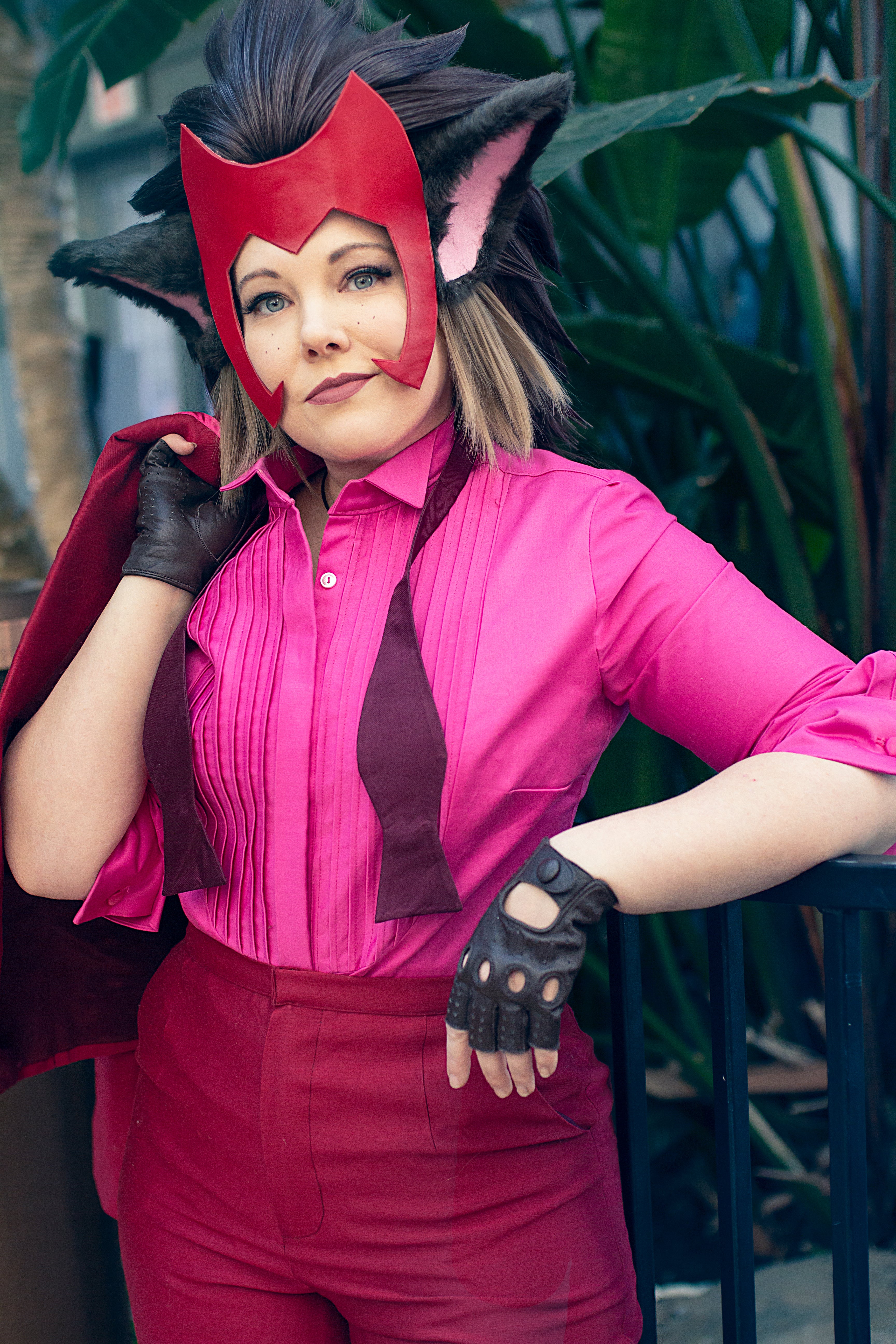 Person in a red and pink superhero costume with a mask, standing outdoors.