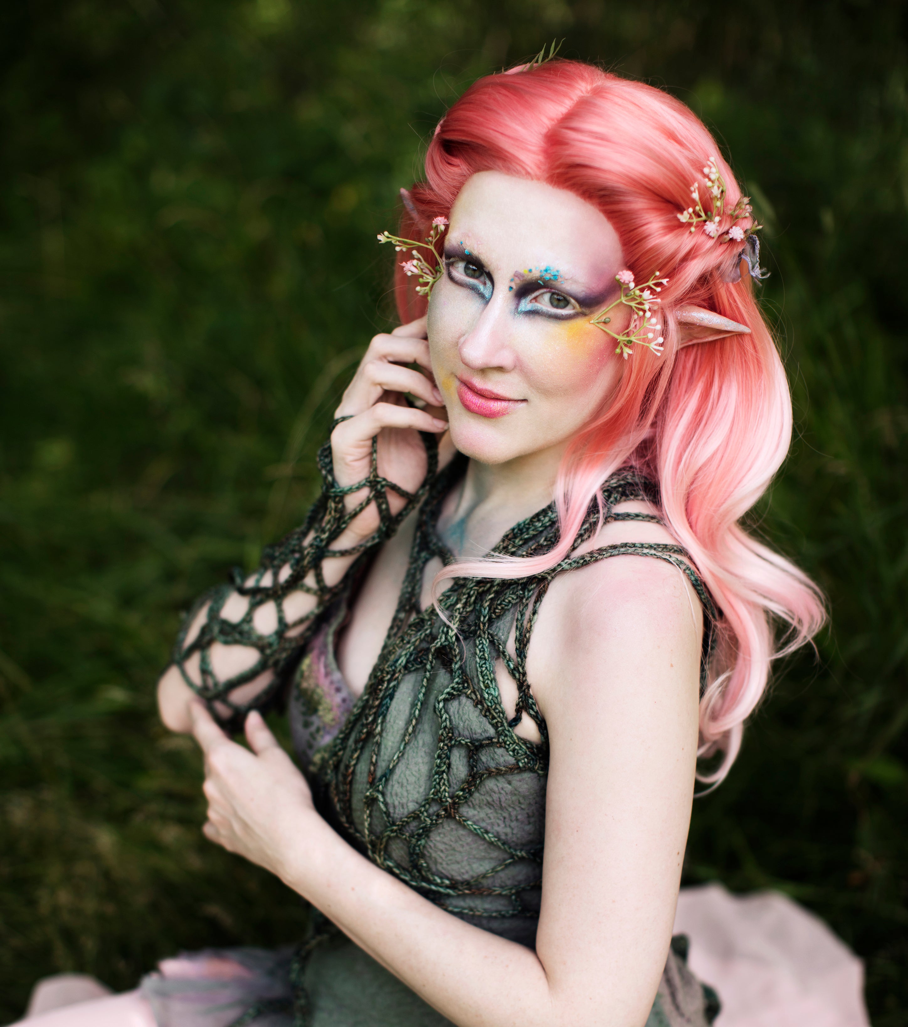 Person with pink hair and fantasy makeup posing outdoors.