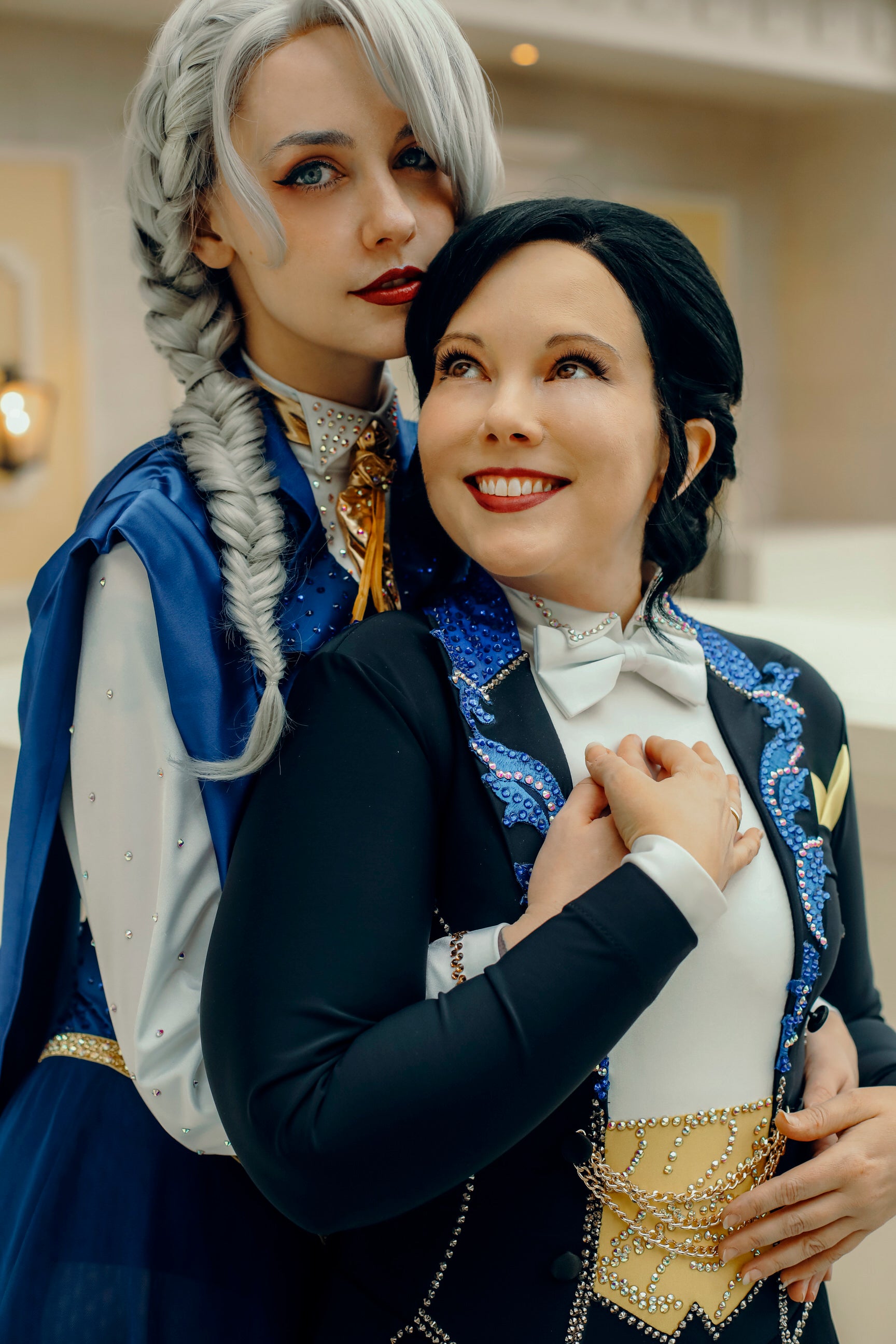 Two people in formal, decorative costumes posing together indoors.
