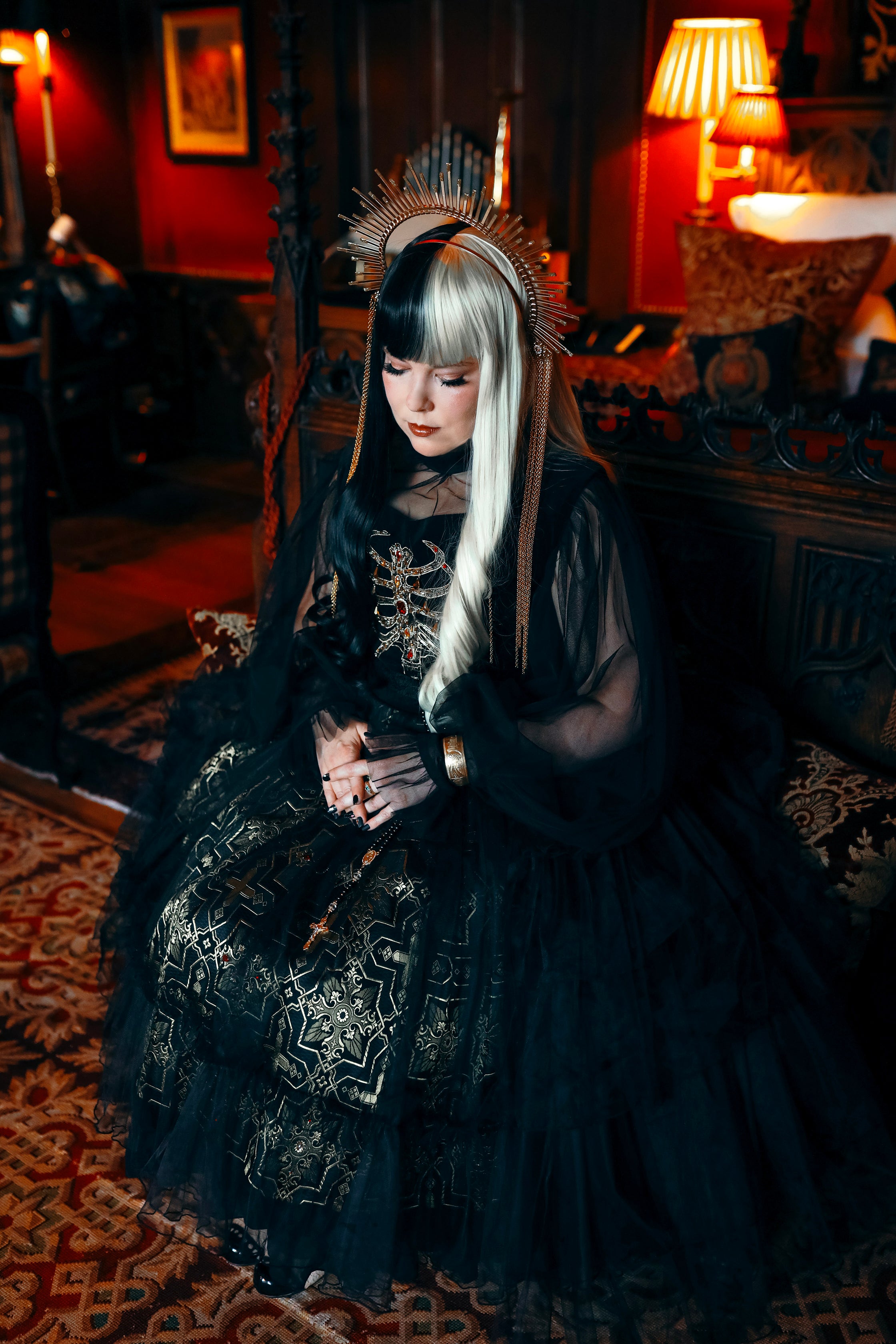 Person in a dark, ornate dress with intricate patterns in a dimly lit room.