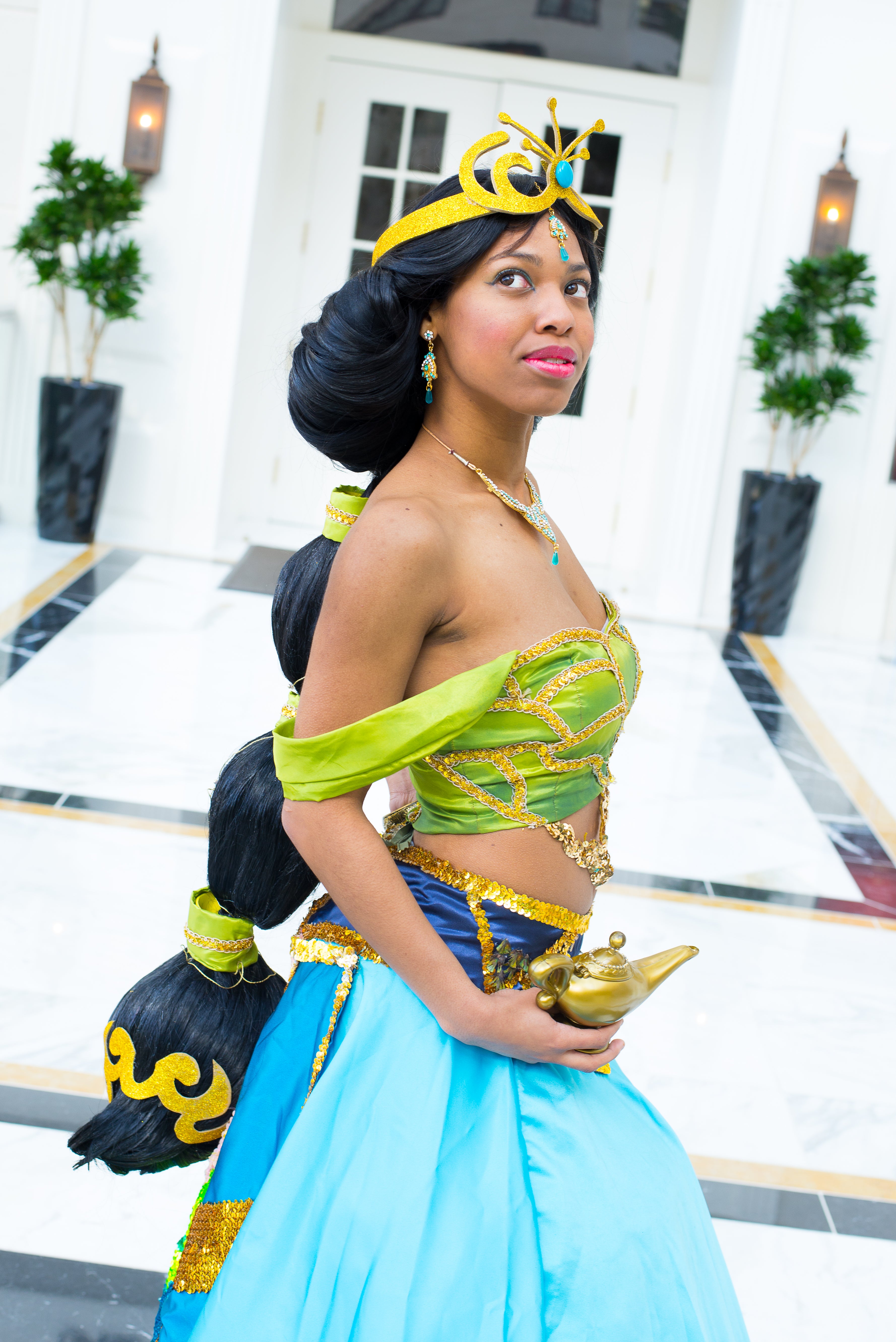 Person in a costume resembling Jasmine from Aladdin, holding a lamp, in an indoor setting.